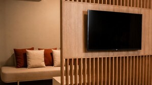 Un dormitorio con cama, televisor montado en un panel de madera, sofá y aire acondicionado instalado en la pared.