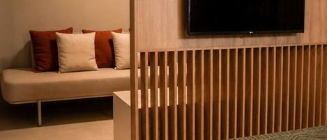 Un dormitorio con cama, televisor montado en un panel de madera, sofá y aire acondicionado instalado en la pared.