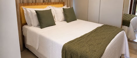 A neatly made bed with white bedding and green pillows, a woven headboard, and a green knitted throw.