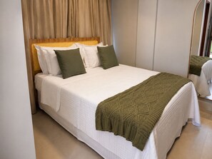 A neatly made bed with white bedding and green pillows, a woven headboard, and a green knitted throw. - BE CAJU FLATS  (Cajueiro da Praia)