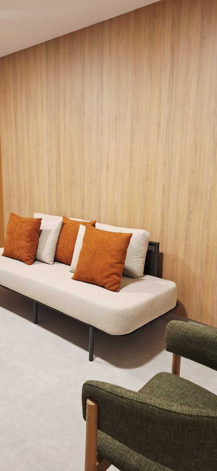 Un sofá con cojines frente a una pared de madera, una silla con asiento de mimbre y un suelo alfombrado.
