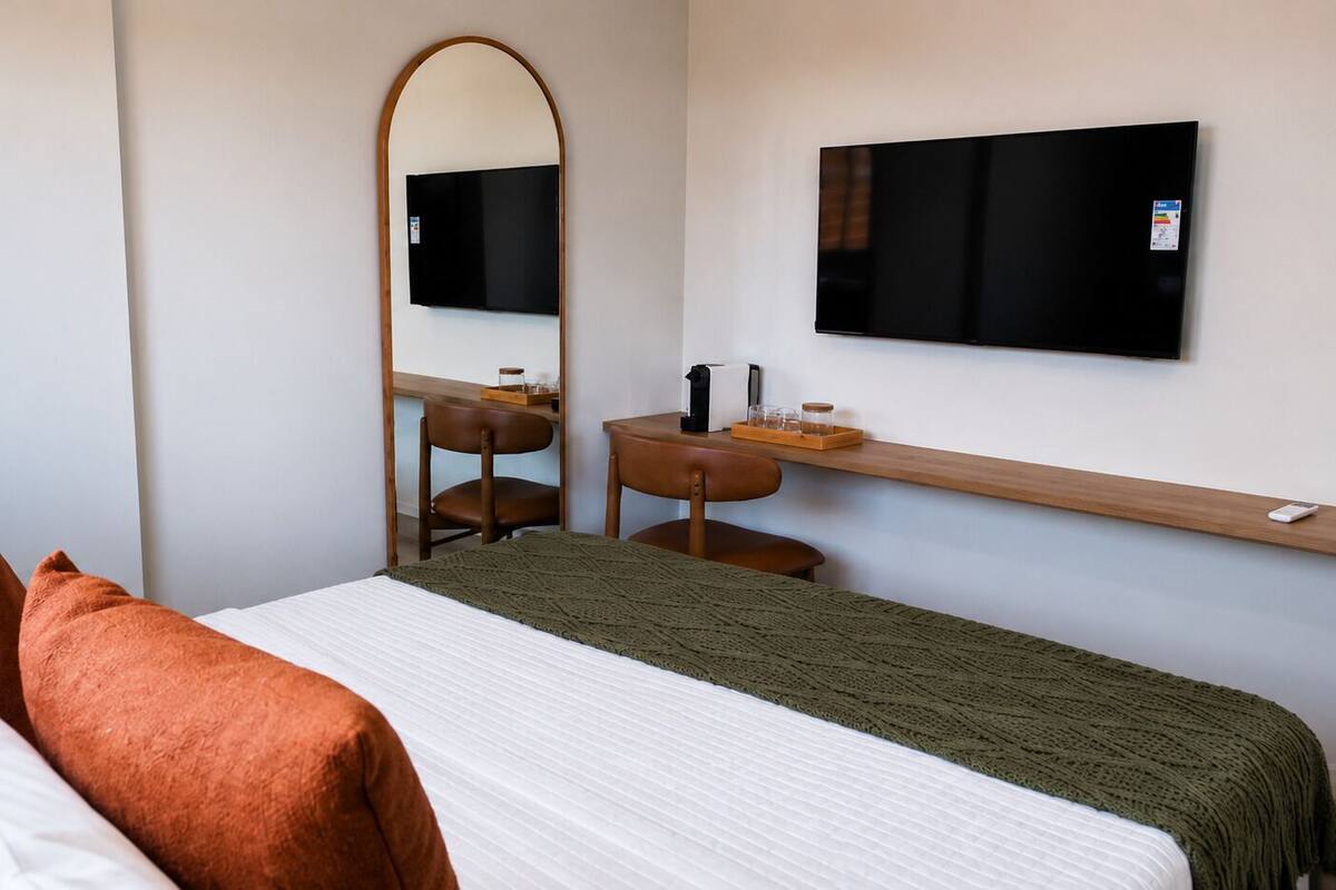 A hotel room with a bed, a desk, a chair, a TV, and a mirror.