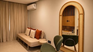 Una habitación moderna con sofá, una silla, una mesita y un espejo grande con marco de madera.