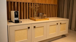 Un mini bar con dispensador de bebidas, un florero de vidrio con flores secas y una bandeja de madera.