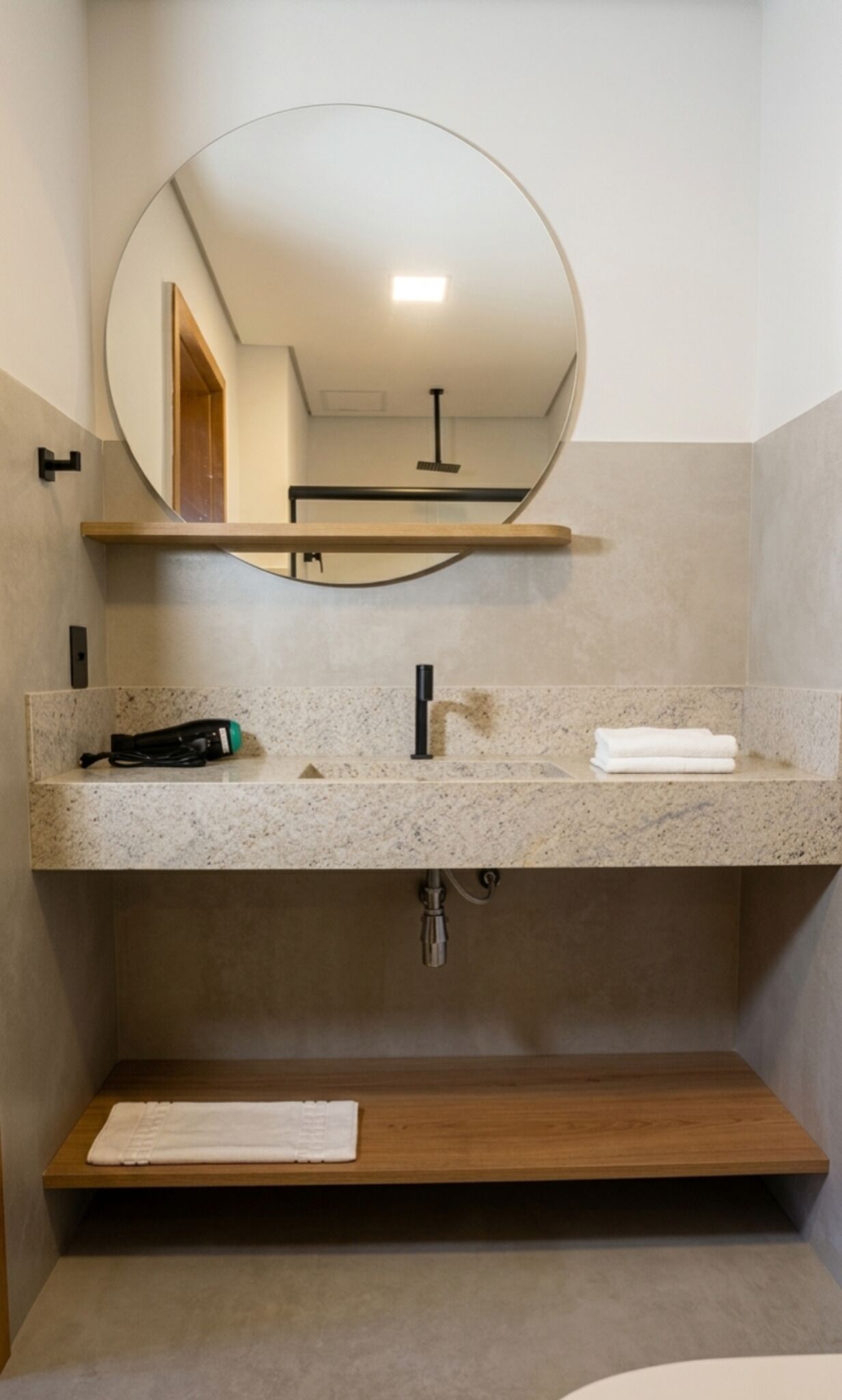 Un baño con un espejo redondo, un lavamanos con grifo, un perchero y una estantería.
