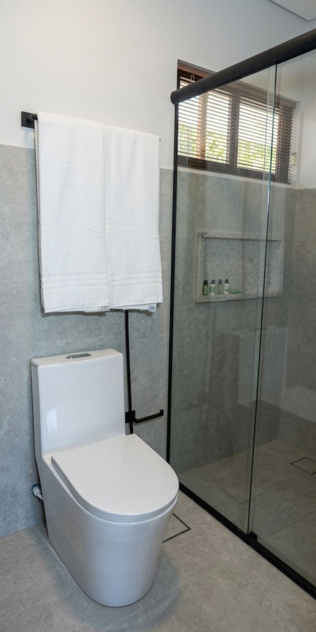 Un baño con inodoro, cabina de ducha de cristal y perchero para toallas.