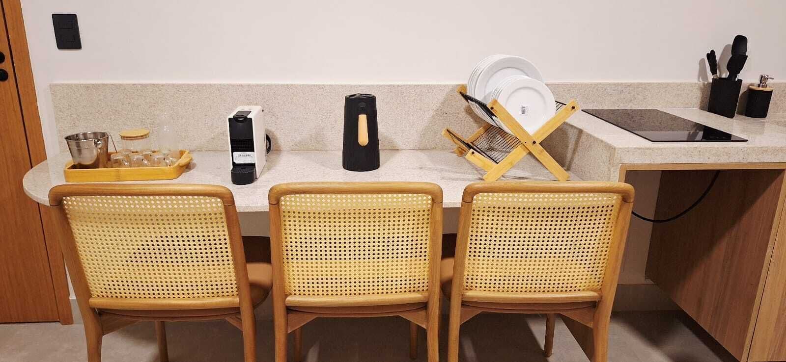Une cuisine avec trois chaises en osier, un égouttoir, une machine à café et un évier.