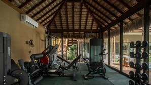 Un gimnasio con equipo de ejercicio, un muro espejado y un techo de paja.