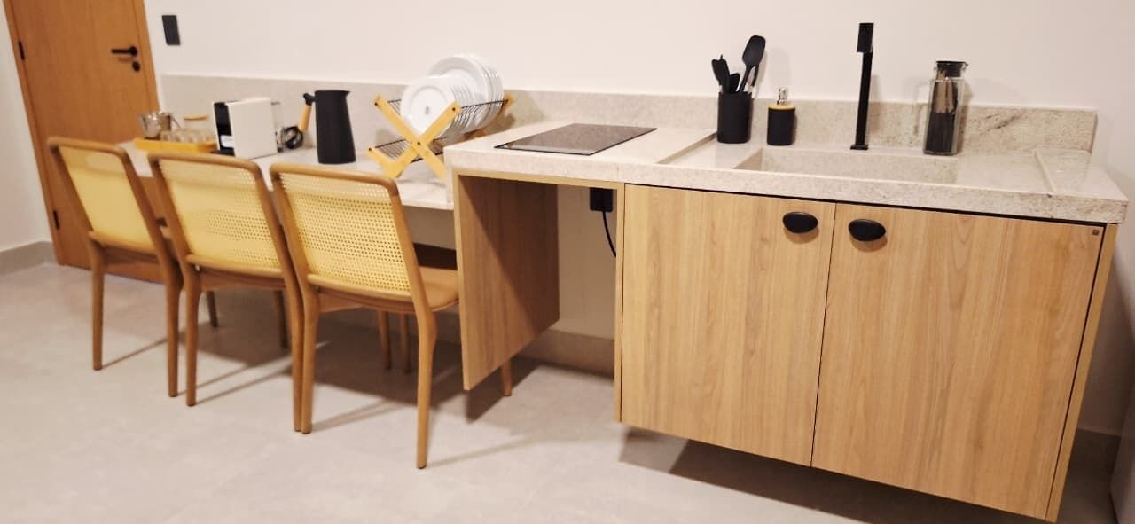 Una cocina con armarios de madera, una encimera, un fregadero y una zona de comedor con sillas.