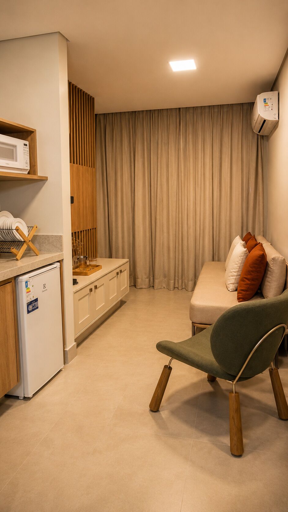Un espacio habitable compacto con kitchenette, comedor y zona de estar con sofá y sillón.
