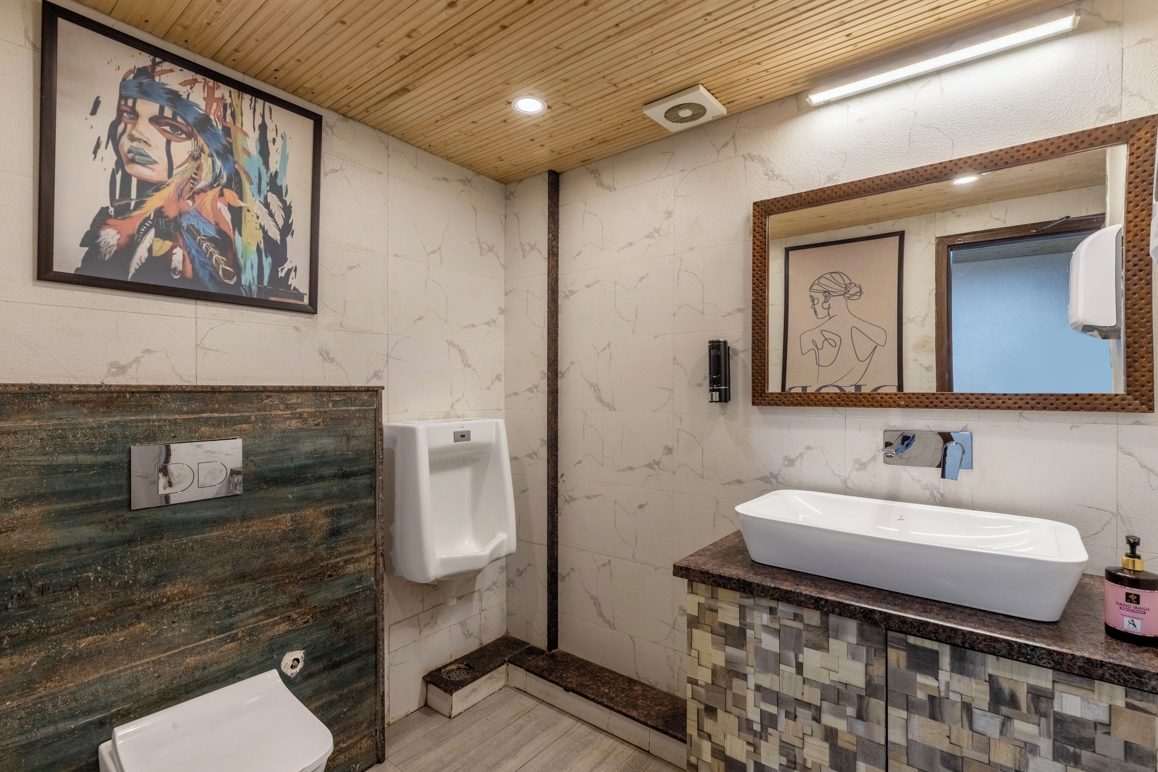 Un baño con pared de mármol, techo de madera, un orinal, un lavabo y una obra de arte enmarcada.
