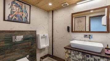 Un baño con pared de mármol, techo de madera, un orinal, un lavabo y una obra de arte enmarcada.
