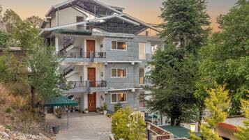A multi-story building with balconies, a stone pathway, and surrounding greenery.