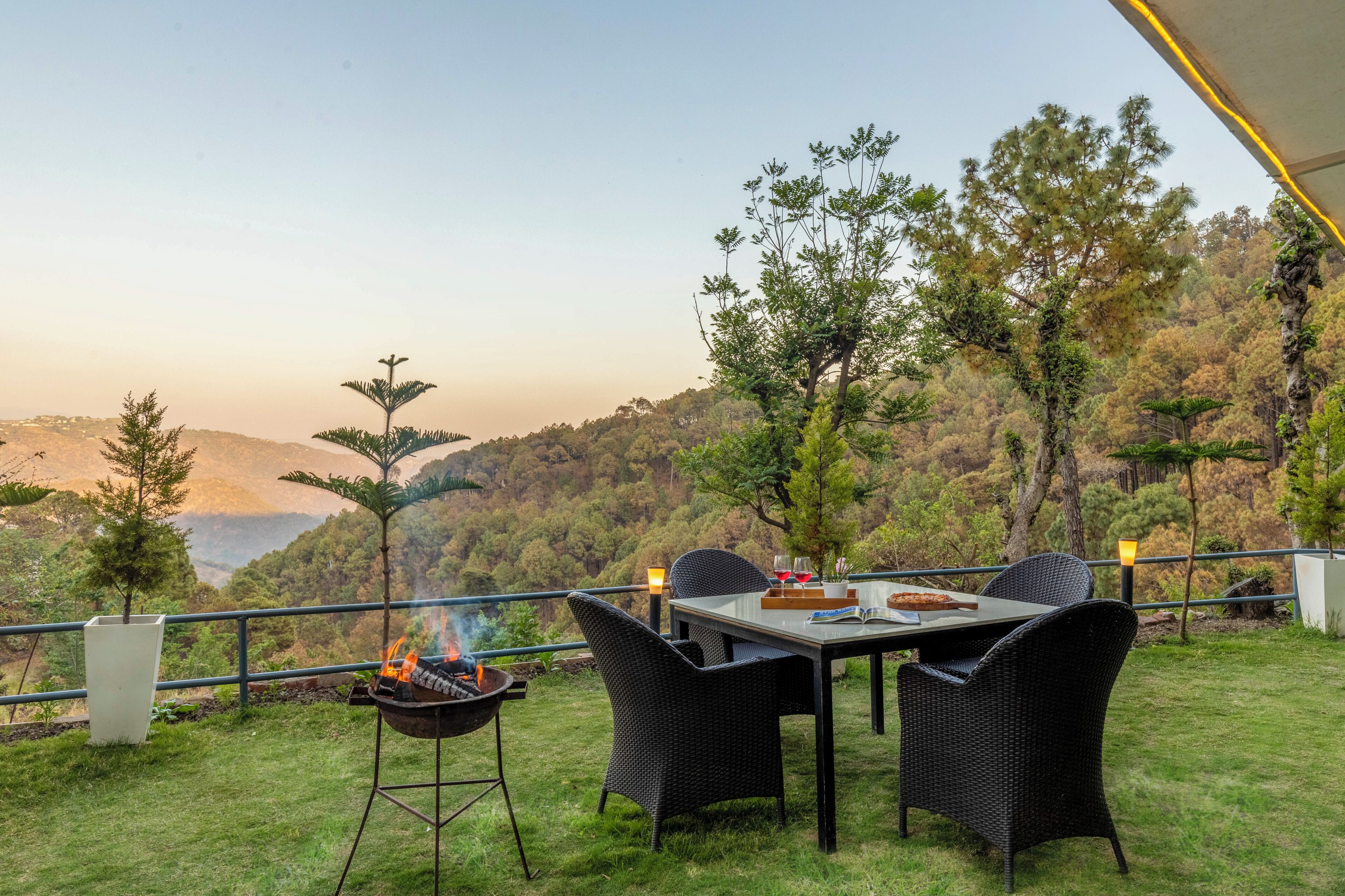 An outdoor dining area with a table and chairs, a grill, and a view of a mountainous landscape.