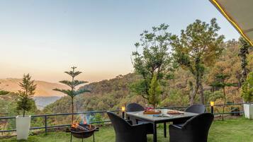 An outdoor dining area with a table and chairs, a grill, and a view of a mountainous landscape.