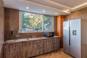 A modern kitchen with a large window, wooden cabinets, a stainless steel refrigerator, and a microwave on the counter.