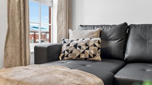 A black leather sofa with a patterned pillow, a beige throw blanket, and a window with curtains. - Apartment Sleeps 6 With Parking (Warrington)