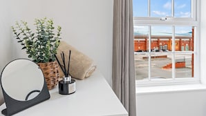 A room with a white desk, a round mirror, a potted plant, a candle, and a towel. - Apartment Sleeps 6 With Parking (Warrington)