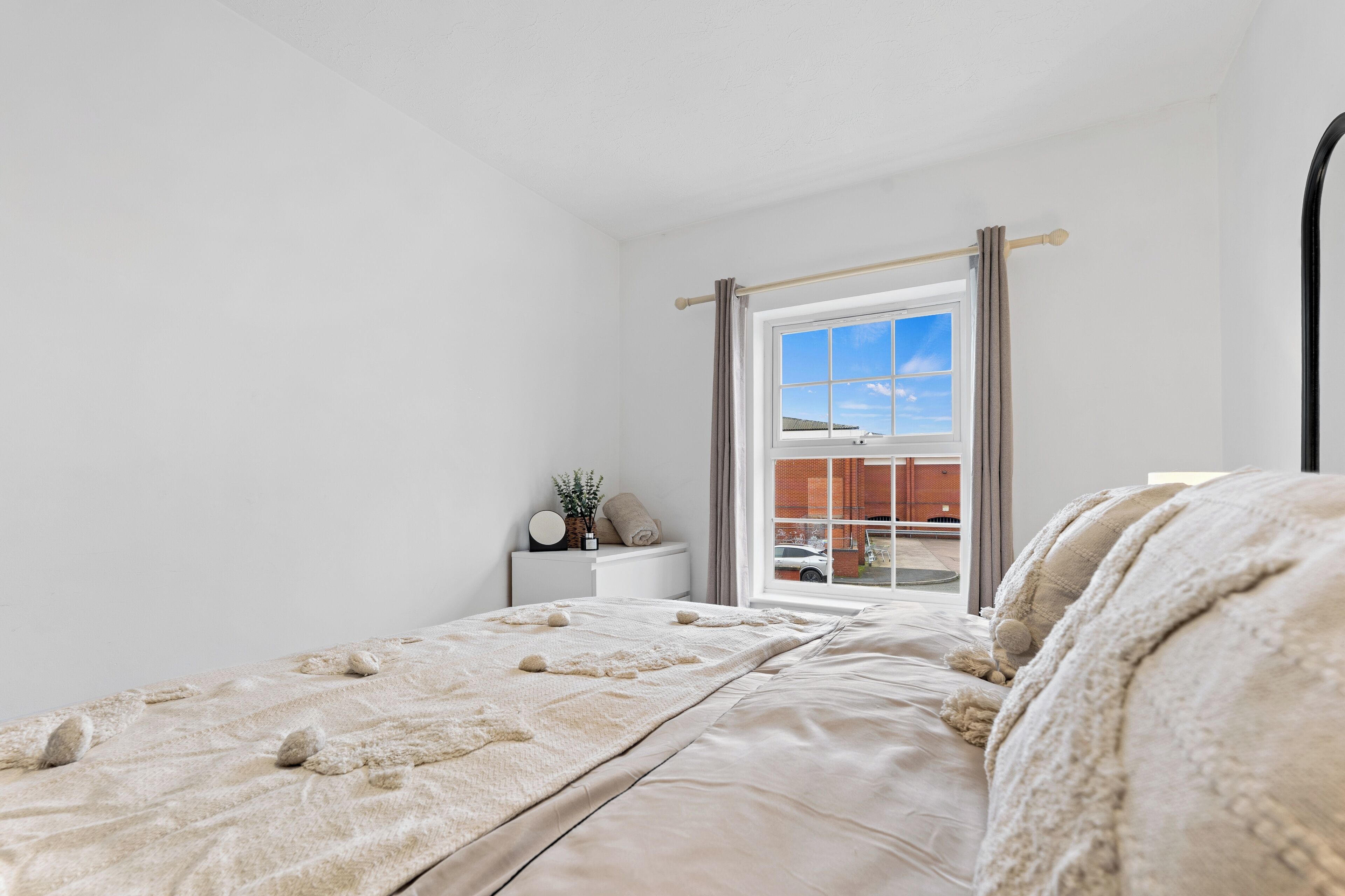 A bedroom with a bed, a nightstand, a window, and a view of the outside.
