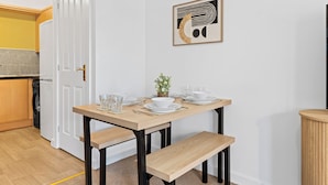 A dining area with a wooden table set for four, a white door, and a kitchen in the background. - Apartment Sleeps 6 With Parking (Warrington)