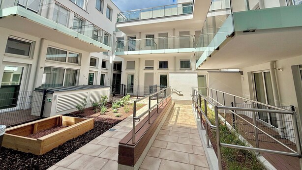 A multi-level residential building with balconies, a central courtyard with a wooden planter, and a staircase leading to the upper floors. - Business Quartier Belvedere (Vienna)