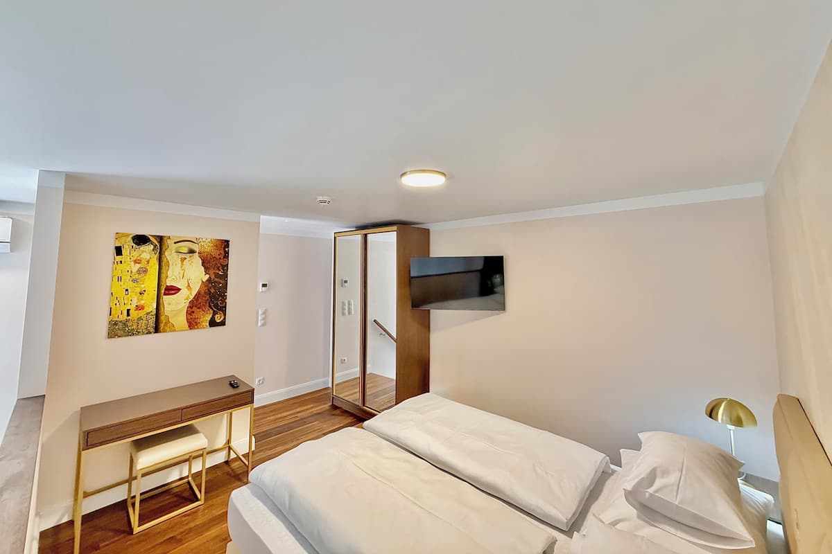 A modern hotel room with a bed, a desk, a painting, and a TV.