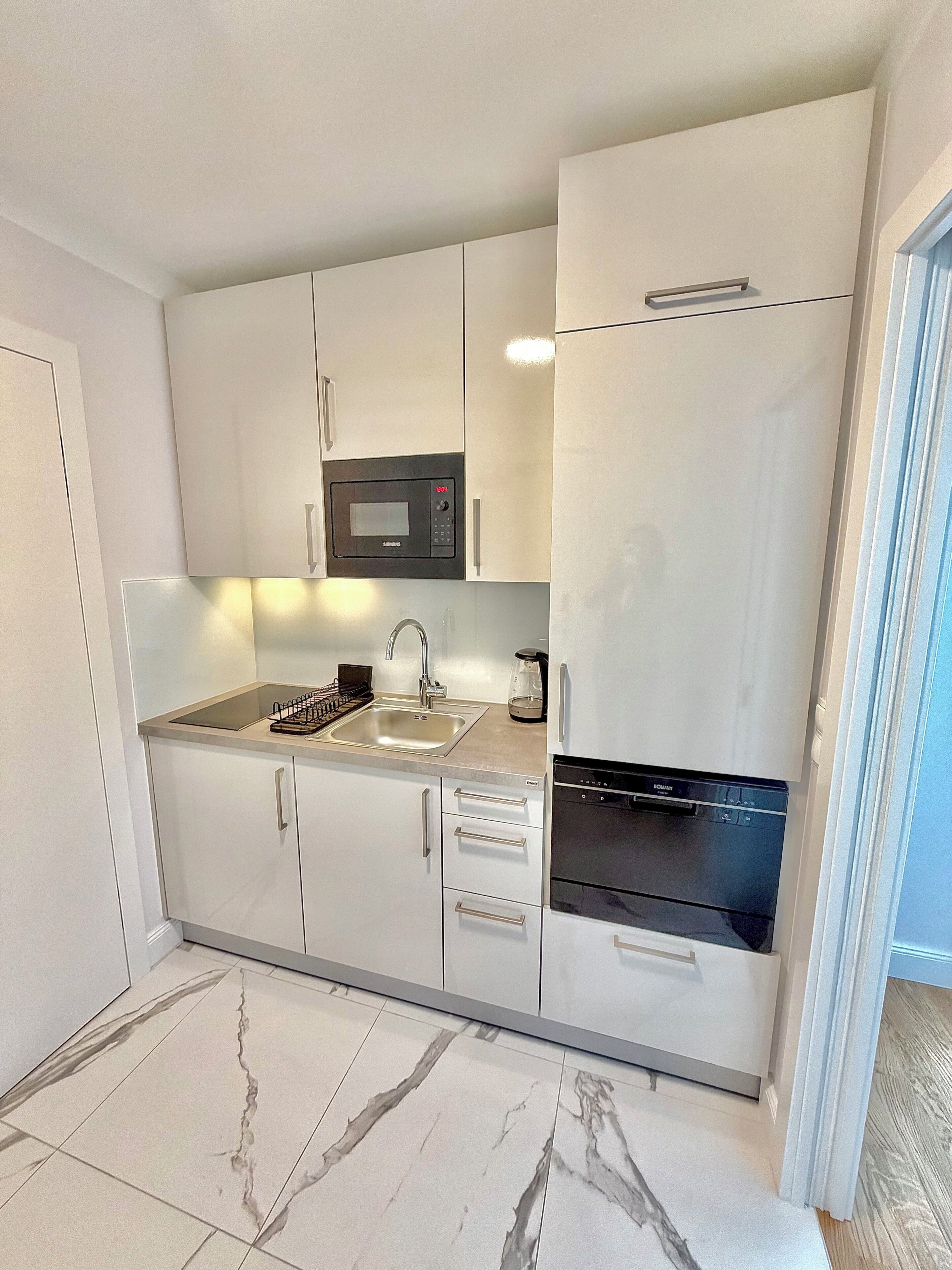 A compact kitchen with white cabinets, a built-in microwave, a sink, and a dishwasher.