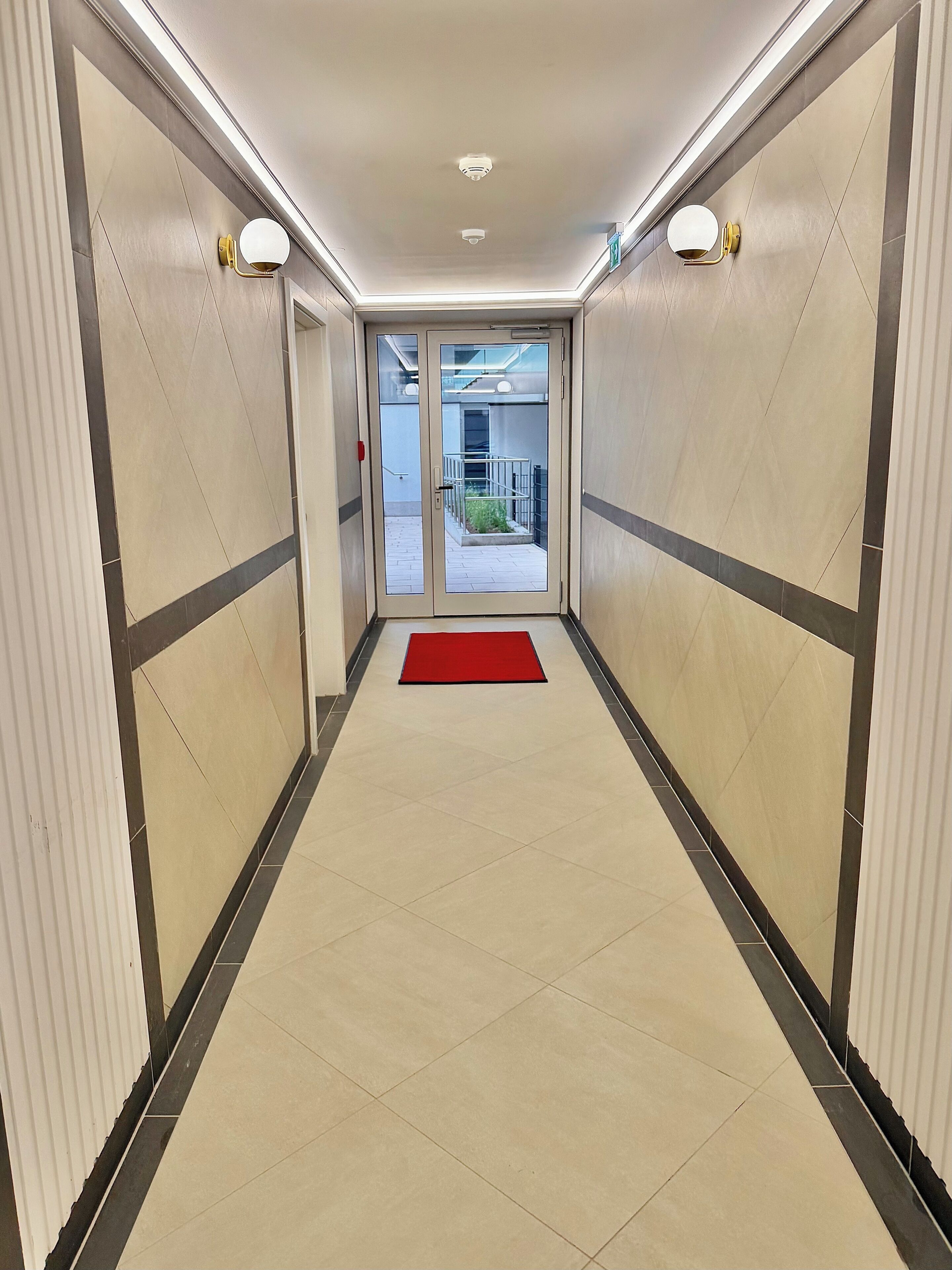 A hallway with a red carpet, tiled walls, and a door leading to an outdoor area.