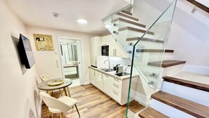 A modern kitchen with white cabinets, a glass staircase, and a dining area with a round table and chairs. - Business Quartier Belvedere (Vienna)