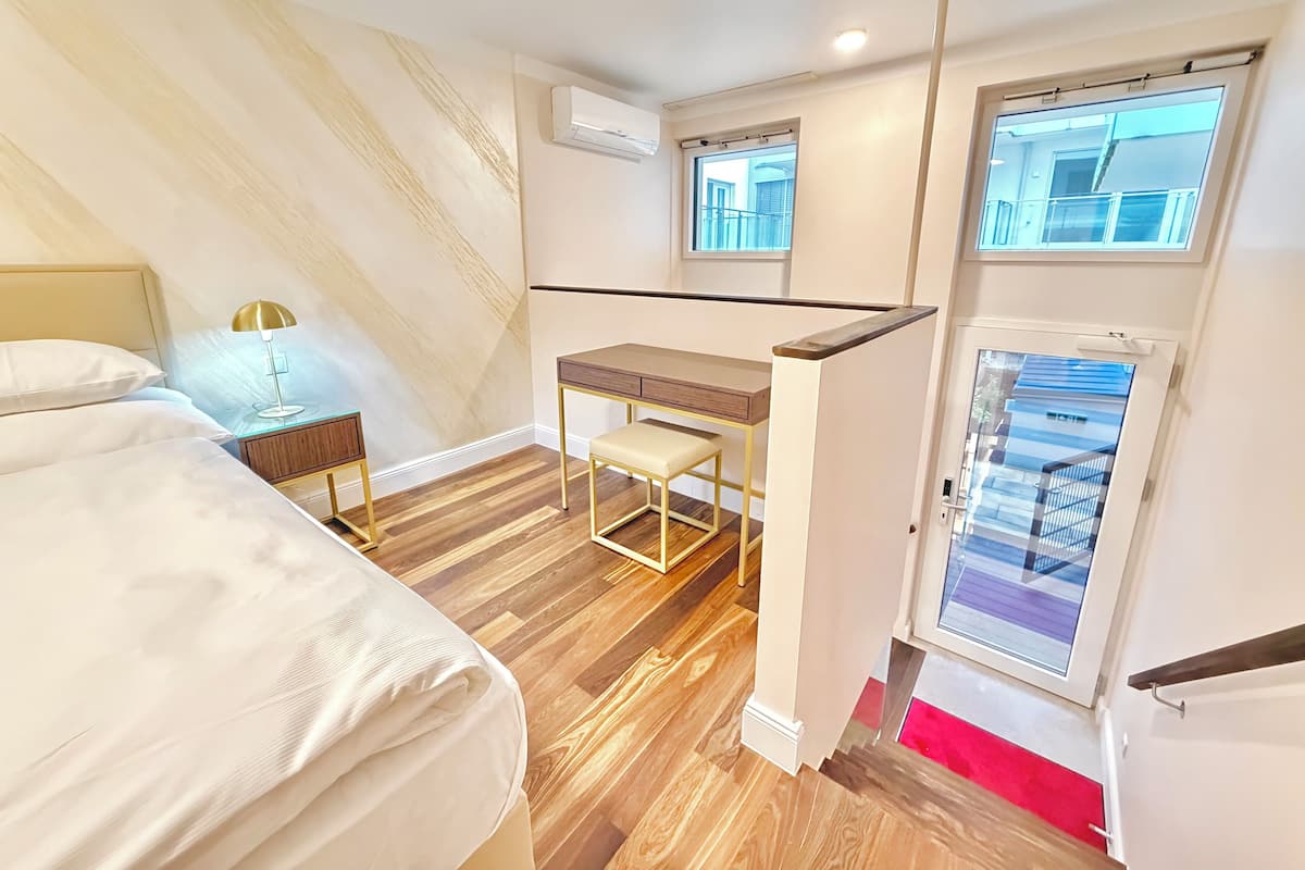 A hotel room with a bed, a desk, a chair, a lamp, and a window with a view.