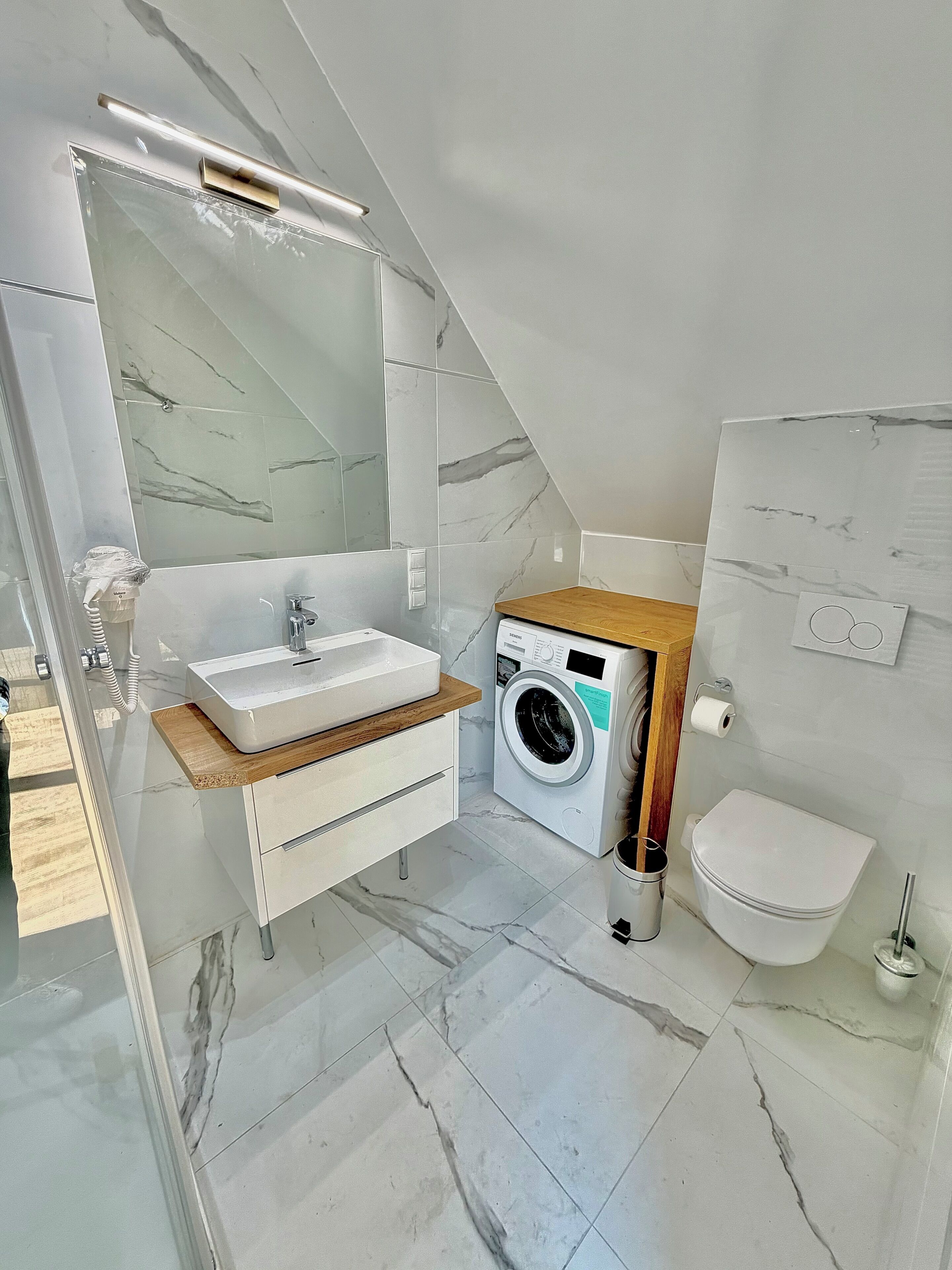 A modern bathroom with a marble floor, a built-in sink, a washing machine, and a toilet.