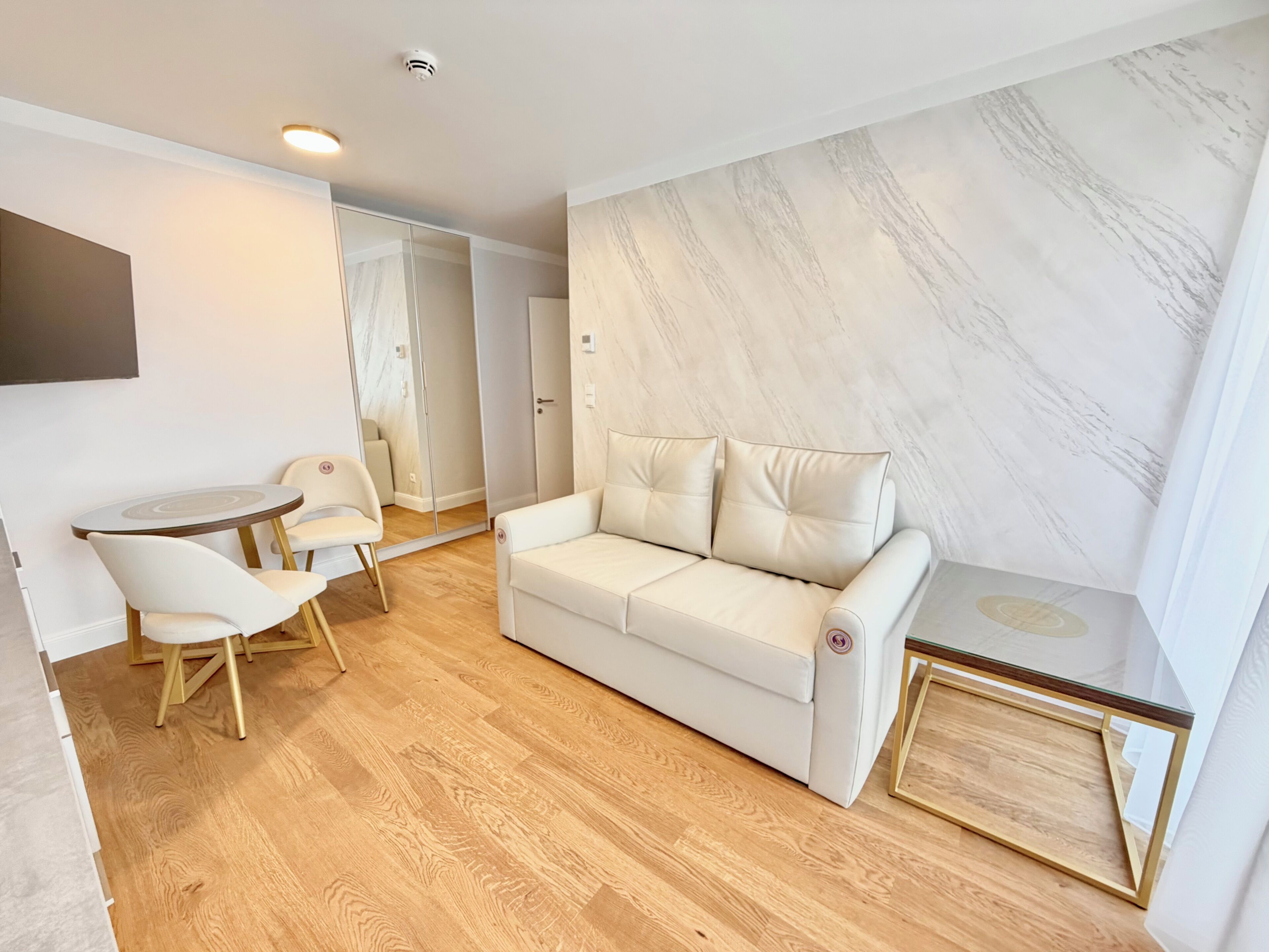 Una sala moderna con un sofá blanco, una mesita redonda y dos sillas.