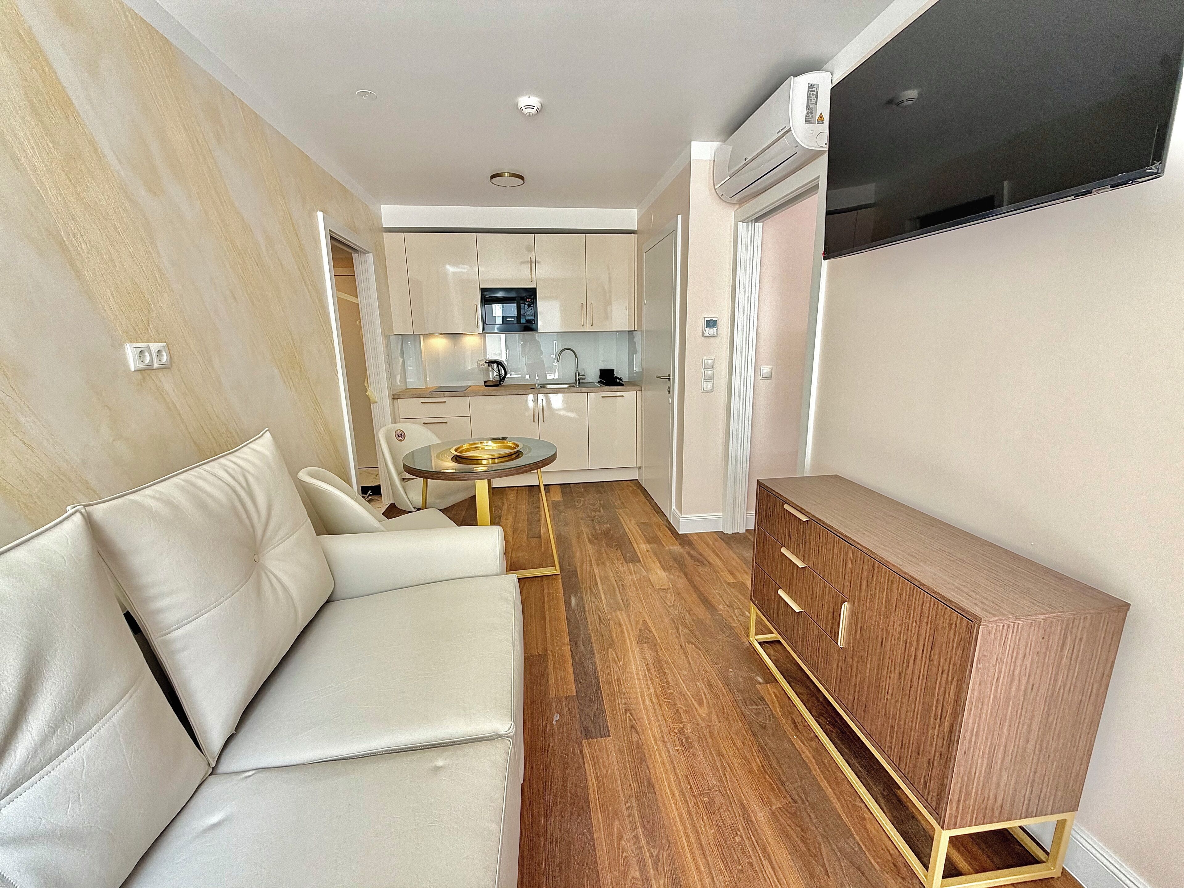 A modern living area with a sofa, a small round table, a wooden cabinet, and a kitchen in the background.