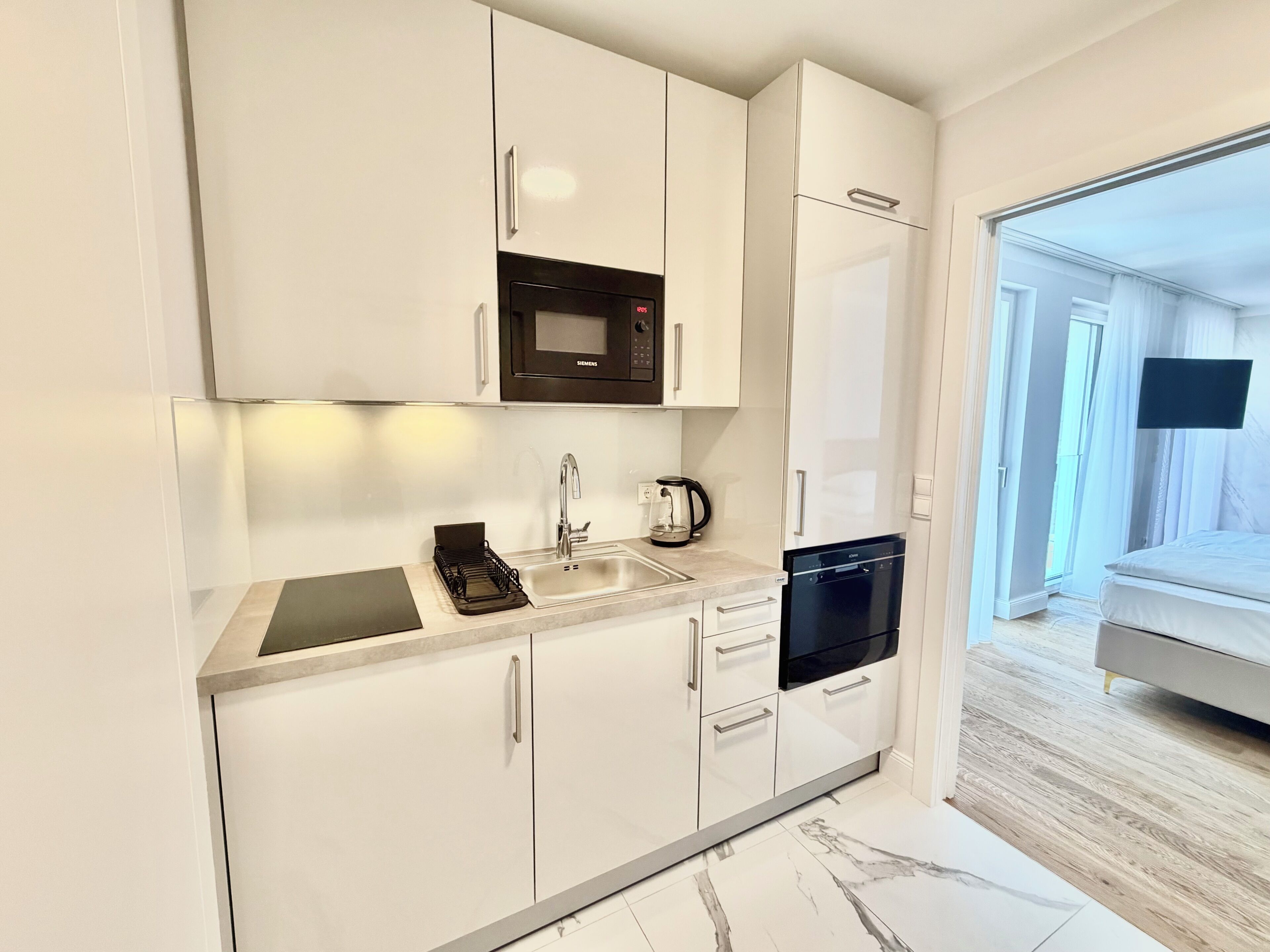 A modern kitchen with white cabinets, a black microwave, a coffee maker, and a dishwasher.