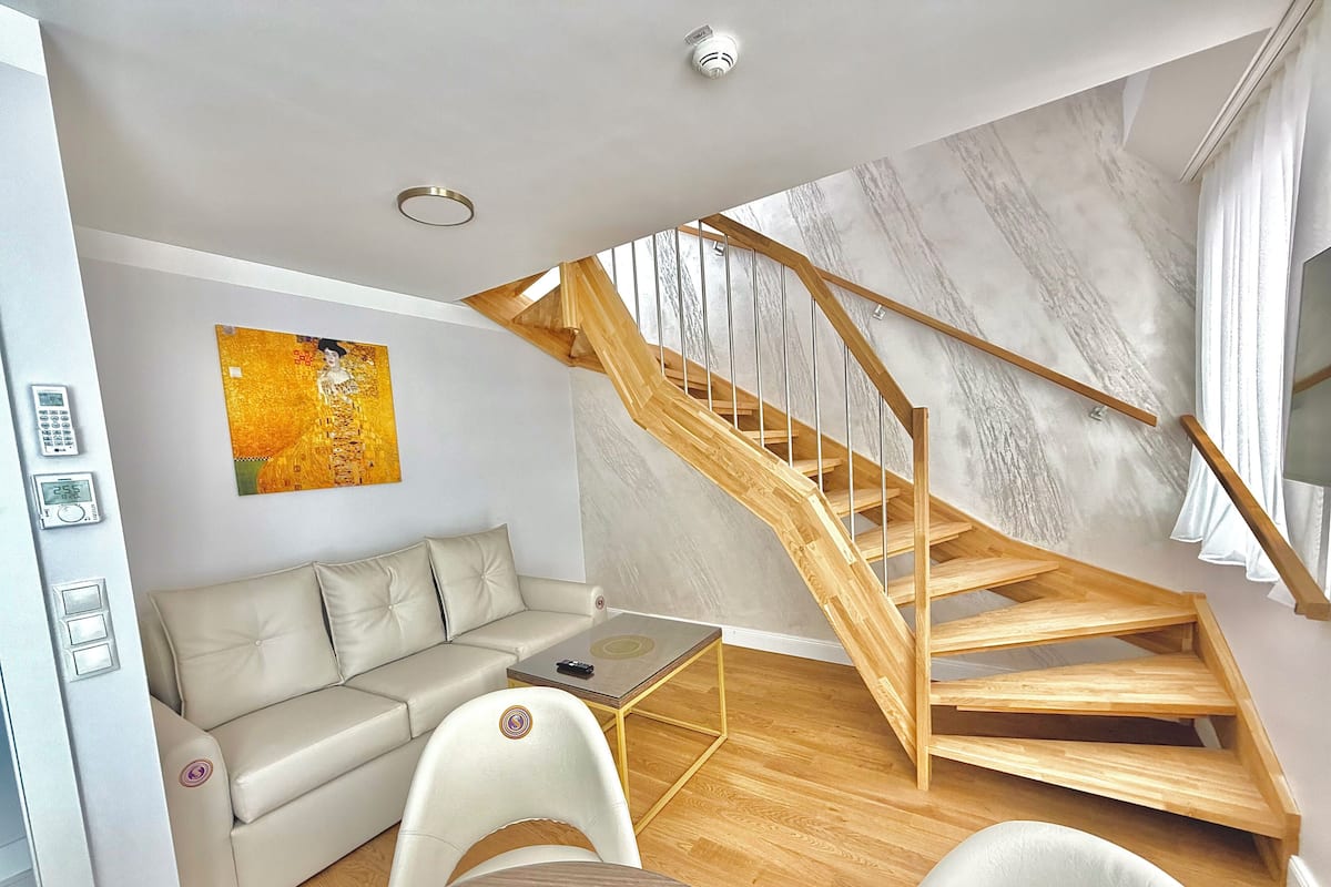 A modern living room with a wooden staircase, a sofa, a coffee table, and a painting on the wall.