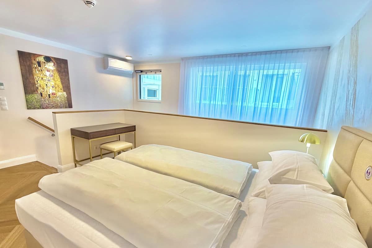 A hotel room with two beds, a desk, a chair, a window with curtains, and a painting on the wall.