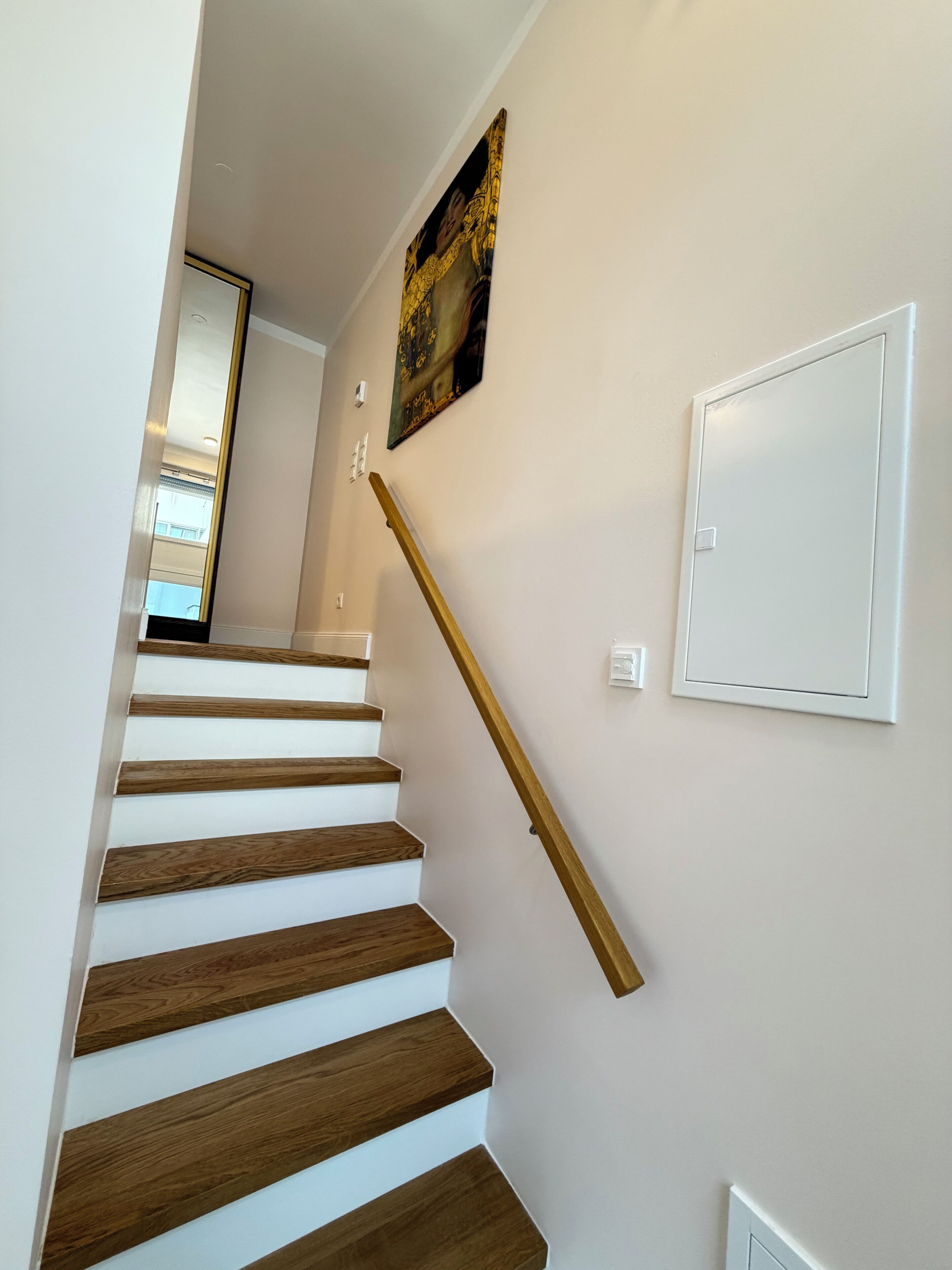 A staircase with wooden steps and a handrail, a wall-mounted light switch, and a framed picture.
