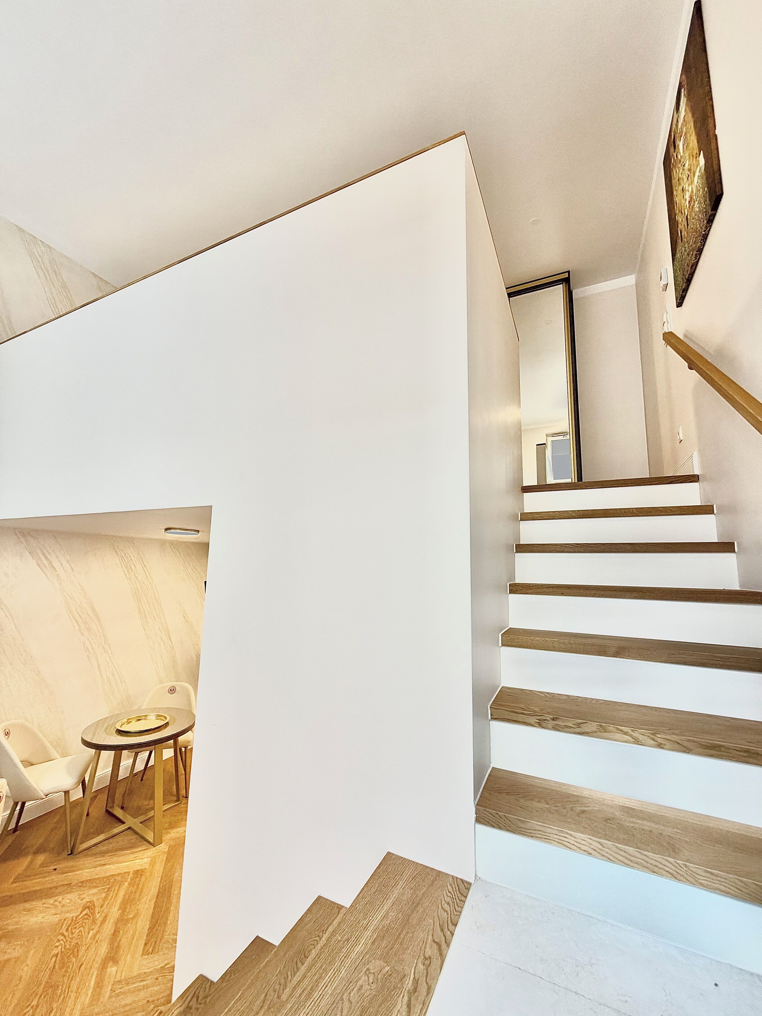 A modern interior with a staircase, a dining area with chairs and a table, and a large mirror.