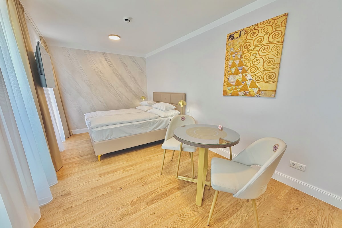 A bedroom with a bed, bedside table, chair, and a wall-mounted artwork.