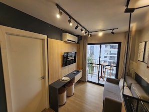 Ein kompakter Wohnraum mit Küchenzeile, einer Couch, einem Esstisch und einem Balkon mit Blick auf Gebäude.