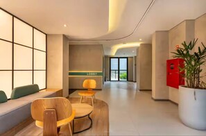 Eine moderne Lobby mit Sitzgelegenheiten, einem Empfangstresen mit der Aufschrift 'Lobby' und einer Zimmerpflanze.
