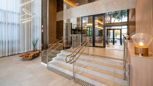 A modern hotel lobby with a staircase, a reception desk, and a large glass door leading to the outside. - Studio Bem Localizado - Moema (São Paulo)