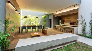 A modern outdoor kitchen with a dining area, bar stools, and a large planter. - Studio Bem Localizado - Moema (São Paulo)