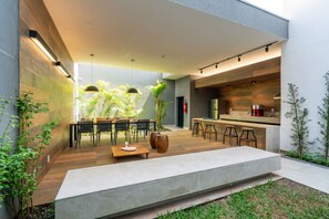A modern outdoor kitchen with a dining area, bar stools, and a large planter. - Studio Bem Localizado - Moema (São Paulo)