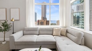 A modern living room with a large window, a grey sectional sofa, a small table, and a floor lamp. - Stylish Marina 1BR with City View, Pool and Gym (Dubai)