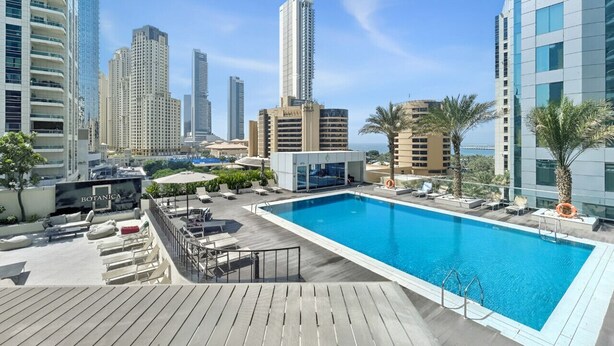 A rooftop pool with a city view, lounge chairs, and a sign reading 'BOTANICA'. - Stylish Marina 1BR with City View, Pool and Gym (Dubai)