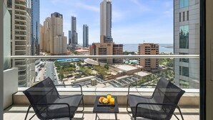 A balcony with two chairs, a table with croissants and orange juice, and a cityscape view. - Stylish Marina 1BR with City View, Pool and Gym (Dubai)