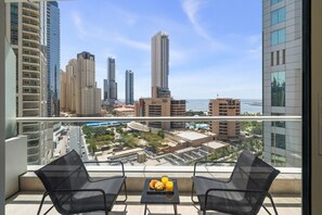 A balcony with two chairs, a table with croissants and orange juice, and a cityscape view. - Stylish Marina 1BR with City View, Pool and Gym (Dubai)