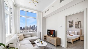 A modern living room with a sofa, coffee table, TV, and a bed with a city view. - Stylish Marina 1BR with City View, Pool and Gym (Dubai)