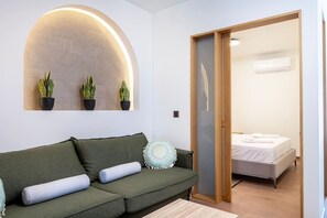 Ein modernes Wohnzimmer mit einem grünen Sofa, einer Wanddekoration und Blick in ein Schlafzimmer mit Bett und Holztür.